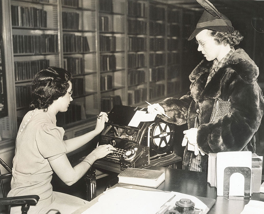 Step 2. After finding the call number in the card catalog for a book the patron wishes to borrow, she requests the book from the library staff member in the Main Reading Room in the Central Library of the Free Library of Philadelphia. 