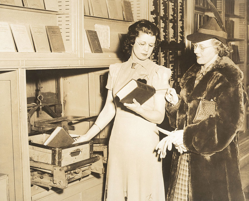 Step 10. In the Main Reading Room of the Central Library of the Free Library of Philadelphia, a library staff member retrieves the requested book from the dumbwaiter and hands it to patron