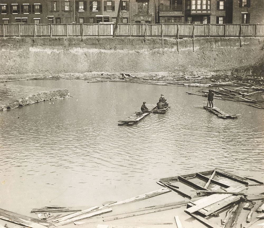 Boys rafting in the water-filled hole excavated for the foundations of the Central Library of the Free Library of Philadelphia, c. 1919